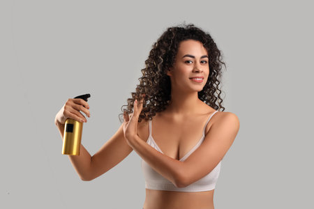 Beautiful African-American woman spraying hair on light backgroundの写真素材