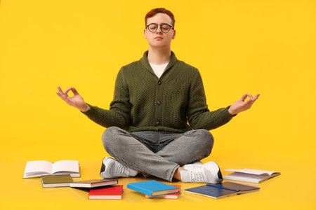 Meditating young man with different books against yellow backgroundの写真素材