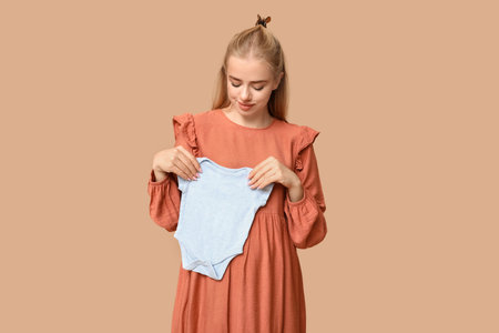 Beautiful happy pregnant woman with baby bodysuit on brown backgroundの写真素材