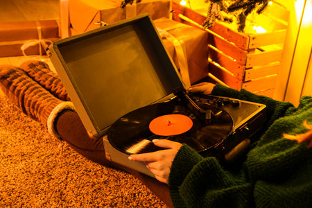 Woman in warm clothes with record player lying on soft carpet in living room at eveningの写真素材