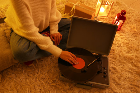 Woman in warm clothes with record player sitting on soft carpet in living room at eveningの写真素材
