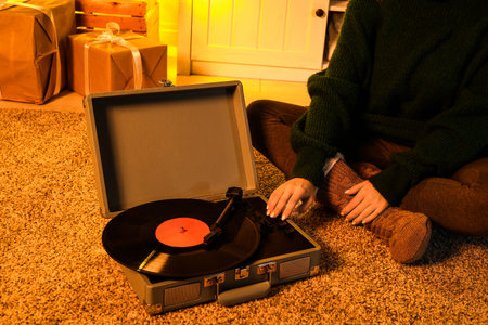 Woman in warm clothes with record player sitting on soft carpet in living room at eveningの写真素材