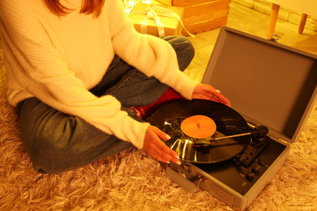 Woman in warm clothes with record player sitting on soft carpet in living room at eveningの写真素材