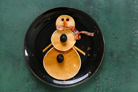 Plate with pancakes in the shape of snowman on green table. Christmas celebrationの写真素材