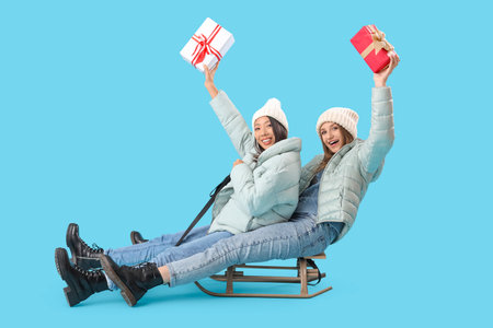 Young women in winter clothes with Christmas gifts sledging on blue backgroundの写真素材