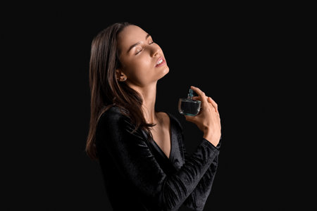 Beautiful young woman applying perfume on dark backgroundの写真素材