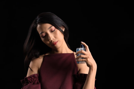 Beautiful Asian woman applying perfume on dark background