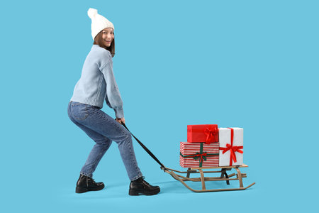 Young woman with Christmas gifts on sledge against blue backgroundの写真素材