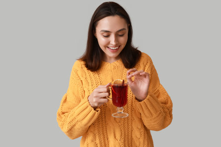 Happy young woman with glass cup of hot mulled wine on gray backgroundの写真素材