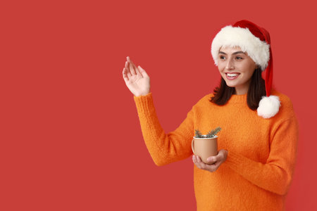 Happy young woman in Santa hat with cup of hot mulled wine on red backgroundの写真素材