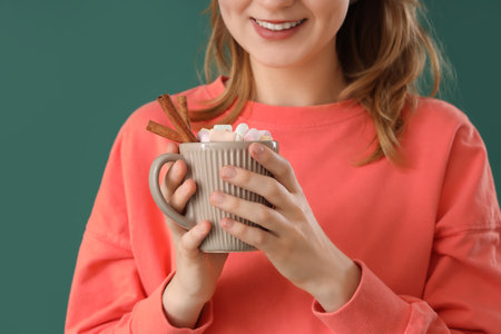 Young woman holding cup of hot chocolate with marshmallows and cinnamon on green background, closeupの写真素材
