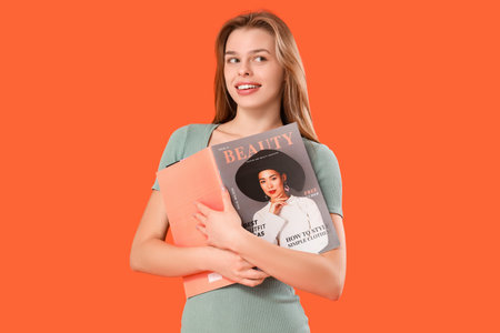 Young woman with magazine on orange backgroundの写真素材