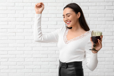 Beautiful young woman with glass of red wine on white brick backgroundの写真素材