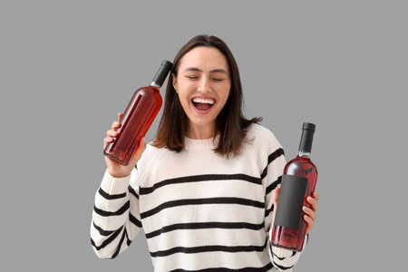 Beautiful young woman with bottles of wine on gray backgroundの写真素材