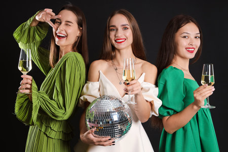 Beautiful young women with champagne and disco ball on dark background. New Year celebrationの写真素材