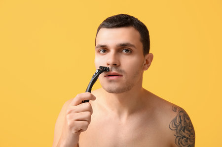 Handsome young man with razor shaving on yellow backgroundの写真素材