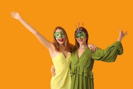 Happy young women in carnival masks on yellow backgroundの写真素材