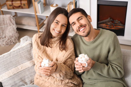 Loving couple holding cups of cocoa with marshmallows at home on winter dayの写真素材