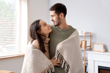 Loving couple with warm plaid at home on winter dayの写真素材