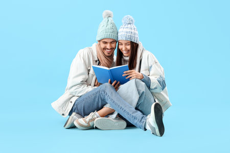 Loving couple in winter clothes reading book on blue backgroundの写真素材