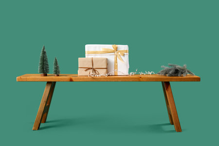 Wooden bench with Christmas presents and toy fir trees on green backgroundの写真素材