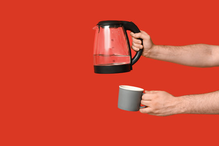 Man with modern electric kettle and mug on red backgroundの写真素材