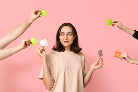 Young woman and hands with condoms on pink background. Safe sex concept