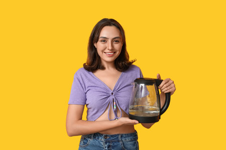 Beautiful young woman with modern electric kettle on yellow backgroundの写真素材