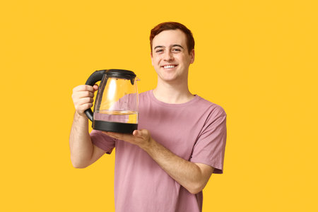Handsome young man with modern electric kettle on yellow backgroundの写真素材