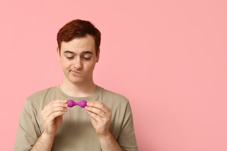 Thoughtful young man with anal plug on pink background