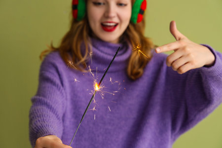 Young woman with sparkler celebrating Christmas on green background