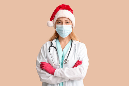 Mature female doctor in Santa hat and medical mask on beige backgroundの写真素材