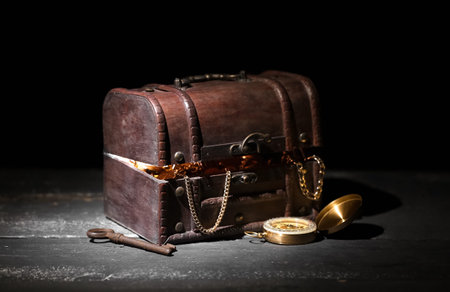 Old chest with treasures, key and compass on wooden table against black backgroundの写真素材