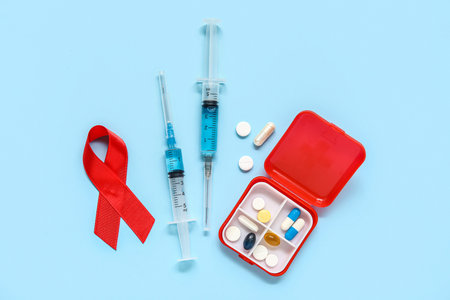 Red ribbon with syringes and pill box on blue background. AIDS Day conceptの写真素材