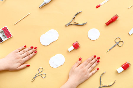 Female hands with stylish red nails and manicure equipment on yellow backgroundの写真素材