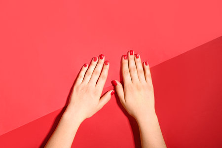 Female hands with stylish red manicure on color backgroundの写真素材