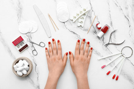 Female hands with stylish red nails and manicure equipment on white grunge backgroundの写真素材