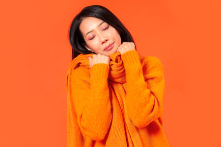 Young Asian woman in warm clothes on orange backgroundの写真素材