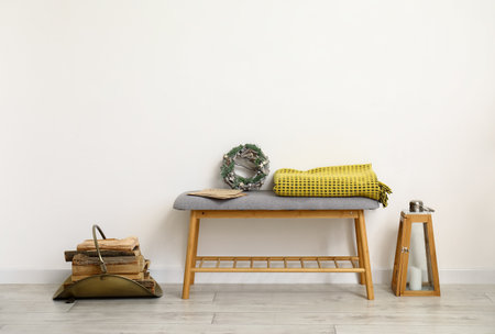 Gray bench with Christmas decor, firewood and warm blanket near white wallの写真素材