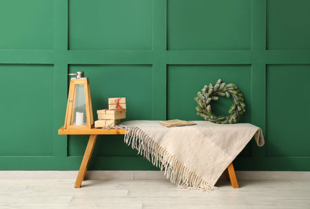 Bench with Christmas wreath, gift boxes and blanket near green wall