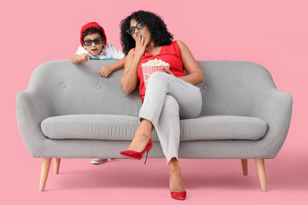 Little boy with his shocked mother in 3D glasses on sofa pointing at viewer against pink backgroundの写真素材