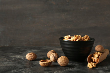 Bowl and scoop of tasty walnuts on table against gray wallの写真素材