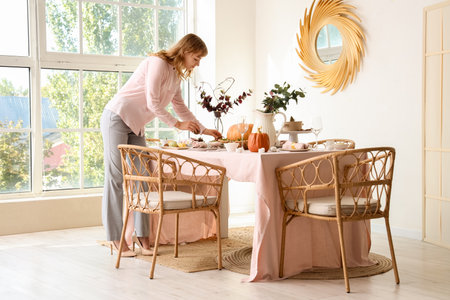 Beautiful young woman decorating table for Thanksgiving Day dinner in dining roomの写真素材
