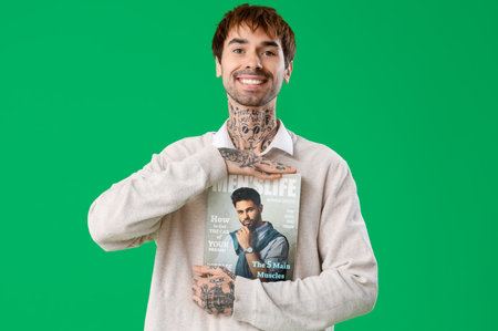 Tattooed young man with magazine on green backgroundの写真素材