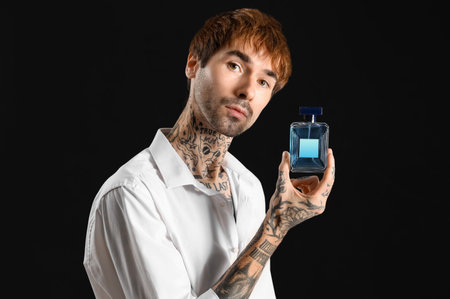Tattooed young man with perfume on dark backgroundの写真素材
