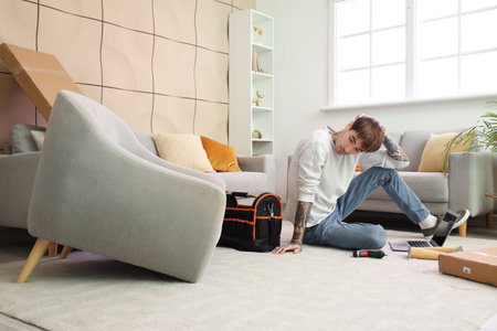 Thoughtful young man assembling furniture at homeの写真素材