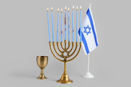Menorah with burning candles, cup and flag of Israel for Hanukkah celebration on gray backgroundの写真素材