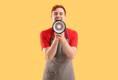 Male confectioner in apron with megaphone on yellow backgroundの写真素材