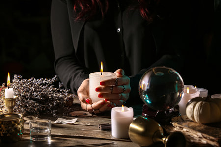 Witch with burning candle at dark wooden table, closeupの写真素材