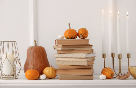 Pumpkins, books and burning candles on mantelpiece in living room, closeupの写真素材